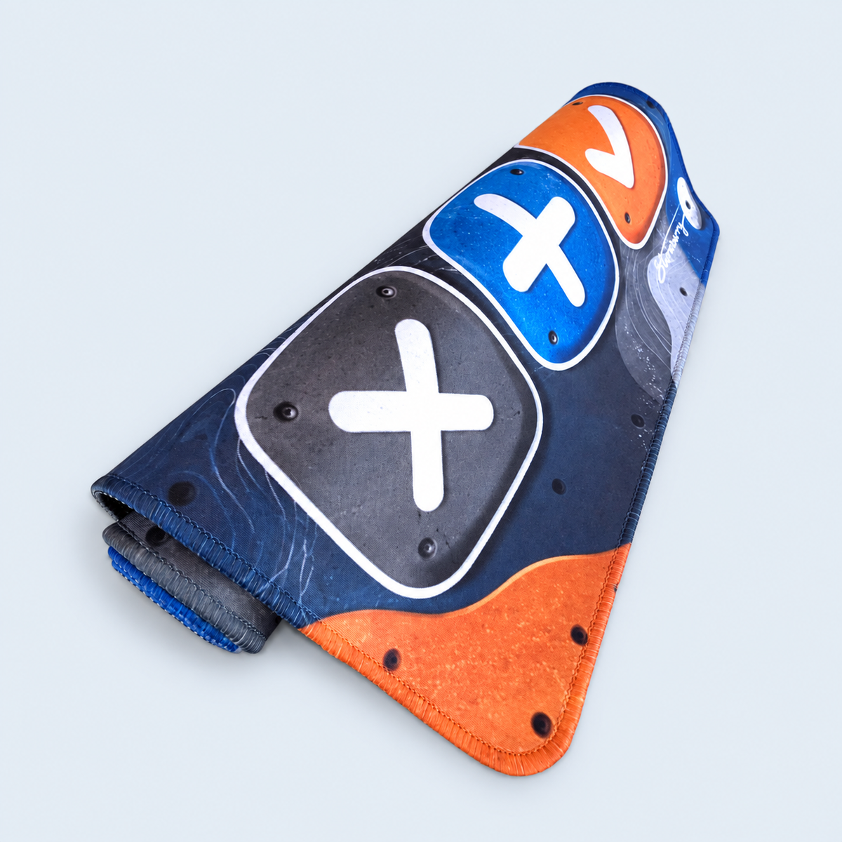XL Boulder Field trading mat loosely rolled, showing its climbing-hold print, blue and orange stitched edges and black rubber backing.
