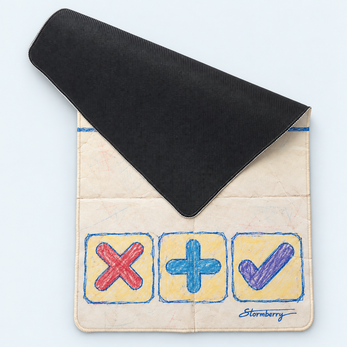 Paper Crayon mat folded back to show its black textured underside and cream face with red X, blue plus and purple check.