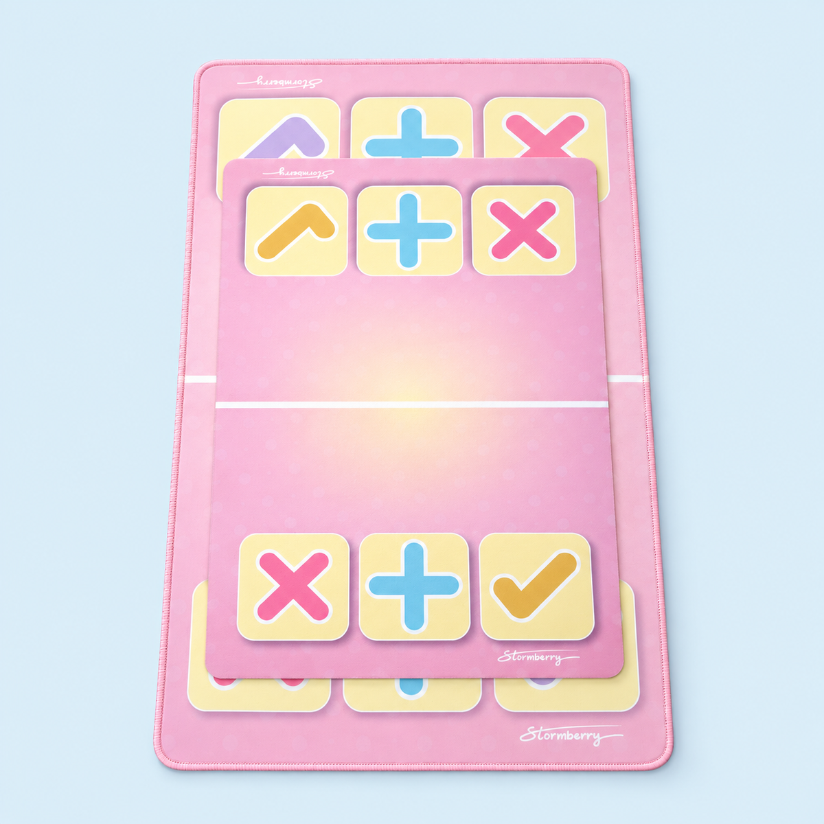 A smaller pink Stormberry trading mat with yellow checks rests on a larger XL pink mat with lavender checks, against a pale blue background.